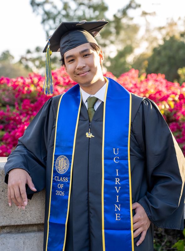 A graduate in a cap and blue stole beside pink flowers