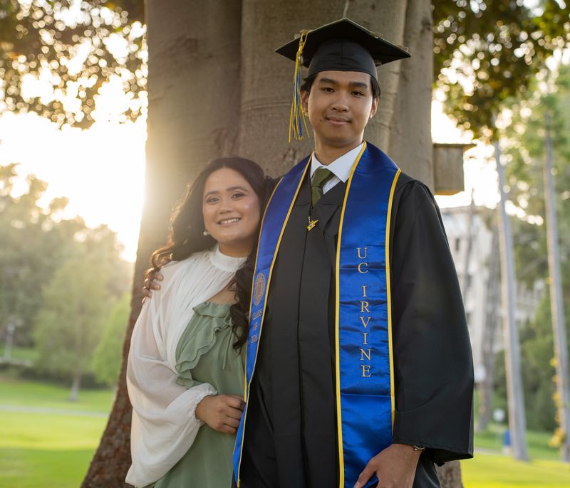 A graduate and a friend under a tree at golden hour
