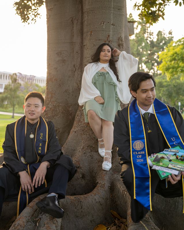 A graduate and a friend posing at the base of a tree