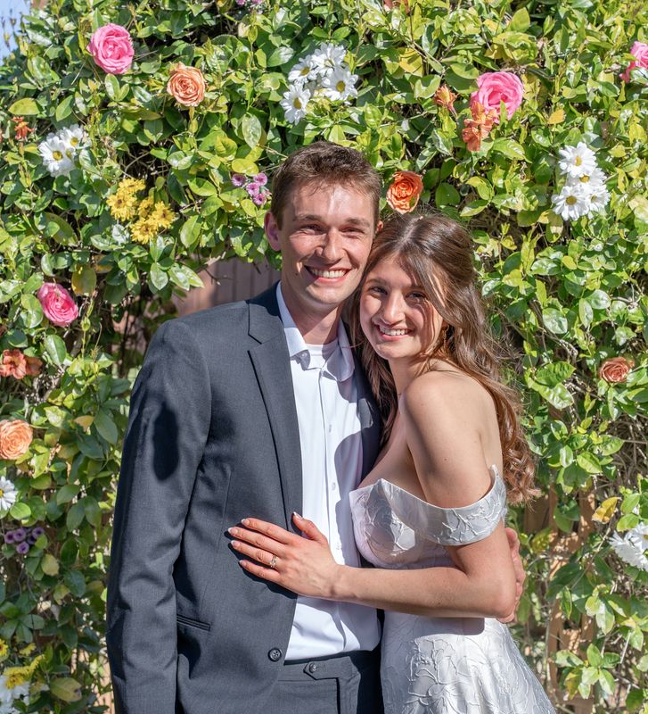 A couple embracing in front of a flower wall