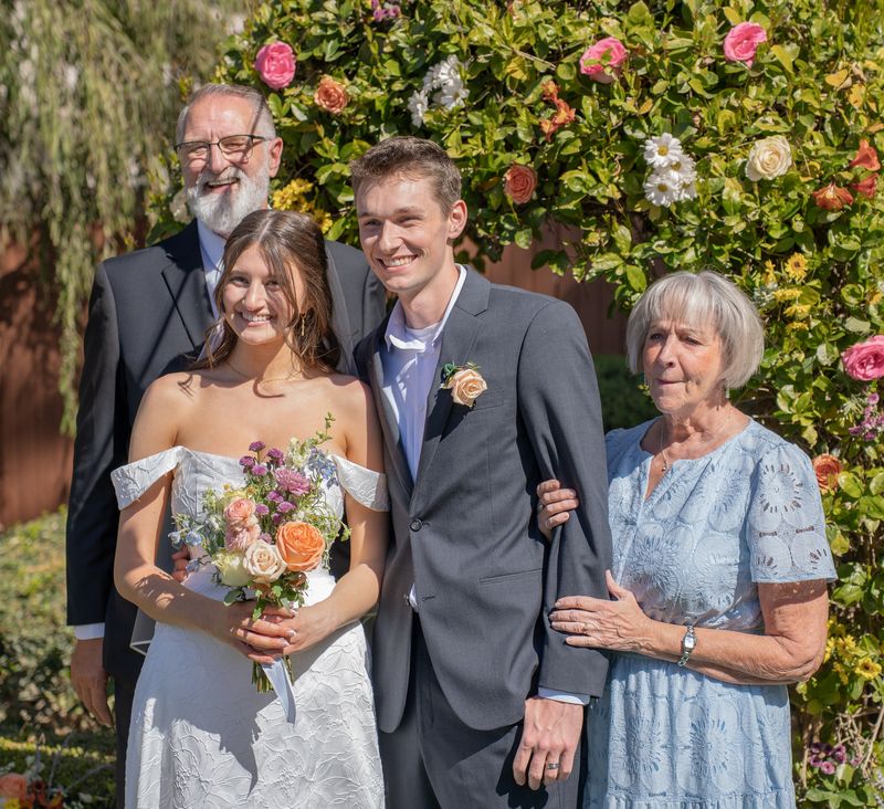 The newlyweds with family in front of a flower wall